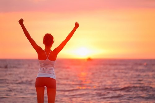 Happy cheering celebrating success woman at beautiful beach sunset. Fitness girl enjoying view with arms raised up towards the sky. Happy free freedom sport concept image outdoors. Biohacking